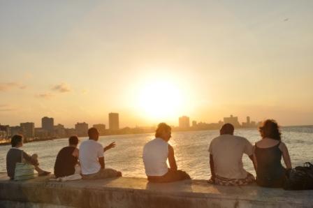 Three American friends sit with three Cuban friends, taking in the sunset together. 