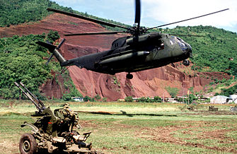 A Sikorsky CH-53D Sea Stallion helicopter of the U.S. Marine Corps hovers above the ground near an abandoned Soviet ZU-23-2 anti-aircraft weapon during the invasion of Grenada in 1983.